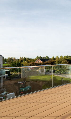Blick von einer Terrasse mit Glasgeländer auf ein modernes Stadthaus und grüne Landschaft in Kiel